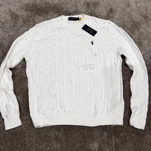 Vit kabelstickad tröja Polo Ralph Lauren - Vit kabelstickad tröja från Polo Ralph Lauren med klassisk rund hals och broderad logga på bröstet. Tröjan är tillverkad i mjuk bomull och har ribbade muddar vid ärmslut och nederkant. Perfekt för dig som gillar clean och stilren look. I always send it same day. Never used!