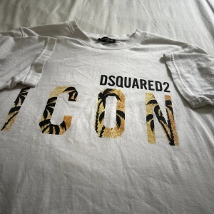 Vit t-shirt  - Vit t-shirt i svart och guld med palmbladsmönster. Klassisk passform, rund hals och korta ärmar. Perfekt statement-plagg för dig som gillar exklusiva märken och snygga detaljer.