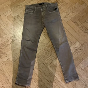 Replay Anbass grå jeans, storlek 32 - Snygga Replay Anbass jeans i grått med klassisk femficksdesign och smal passform. Byxorna har normal midja, raka ben och är tillverkade i mjukt bomullsmaterial med lite stretch för extra komfort. Perfekt för dig som gillar stilrena och moderna jeans. Säljer jeansen för de var tighta för mig. 