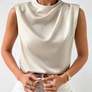Champagnefärgad ärmlös satinblus - Snygg ärmlös blus i champagnefärgad satin med draperad halsringning. Toppen har en rak passform och slät baksida, perfekt för en stilren look. Materialet ger en lyxig känsla och ett mjukt fall.