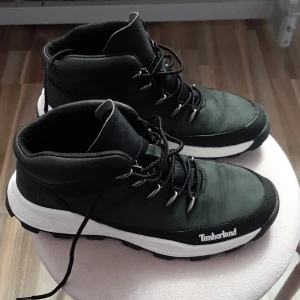 Svarta Timberland kängor med snörning - Säljer ett par svarta Timberland kängor med vit sula och grovt mönstrad yttersula. Skorna har snörning med metallöglor och är tillverkade i slitstarkt skinn och syntet. Perfekta för dig som gillar outdoor och streetstyle. Timberland-logga på sidan och under sulan.