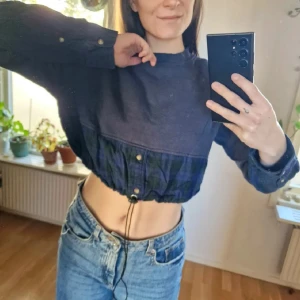 Mörkblå croppad tröja med dragsko - Mörkblå croppad tröja med dragsko i midjan och rutiga detaljer i blått och grönt på ärmar och nederkant. Långa ärmar med knappar och tygen är gosigt och mjukt. Härligt unikt inslag i garderoben 🥰 Mått: Arm - 58, Axelbredd - 45, Längd - 40. Återuppladdad för fri frakt. Jag har mycket annat uppe på sidan, både herr och damkläder. Köp gärna bundle för att få rabatt 🤗 