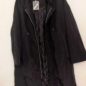 Svart quiltad parkajacka från Stay - Svart parkajacka från Stay i storlek M/L. Jackan har quiltat foder, huva med snörning och dragkedja framtill. Den är lång och har en loose passform, perfekt för dig som gillar oversized stil. Materialet är syntet och jackan har praktiska fickor.