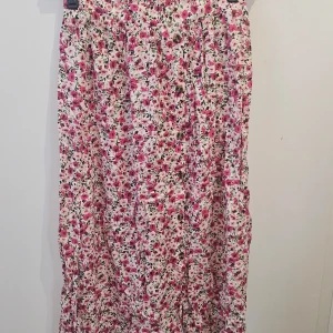 Blommig långkjol med slits och knappar - en långkjol med blommigt mönster i rosa och vitt. Kjolen har en skön passform, slits framtill och vid sidorna och dekorativa knappar. Materialet känns lätt och flowy. helt ny med etiketten