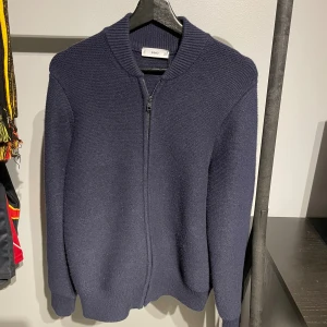 Mörkblå stickad kofta från Mango - Säljer en mörkblå stickad kofta från mango med dragkedja framtill och ribbad krage. enkel och stilren look som funkar till det mesta. väldig varm och sticks inte. passar lätt till en M också.