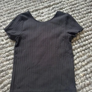 Svart ribbad topp från BikBok - En svart ribbad topp från BikBok med rund halsringning och korta ärmar. Toppen har en enkel och clean look med smala vertikala ränder i tyget. Perfekt att styla med jeans eller kjol för en chill vibe.