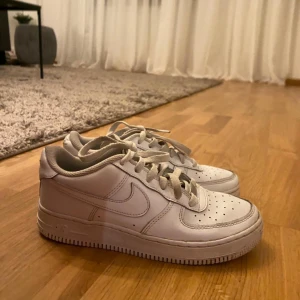 Nike Air Force 1 vita sneakers - Säljer ett par klassiska Nike Air Force 1 sneakers i helvitt skinn. Modellen har låg profil, rund tå och snörning. Snygga perforeringar på tån och den ikoniska swoosh-loggan på sidan. Perfekta för dig som gillar clean och tidlös streetstil.