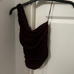 Vinröd oneshoulder topp  - Supersnygg vinröd topp från BikBok i oneshoulder-modell med smal axelrem och draperad effekt. Perfekt för dig som vill sticka ut med en trendig och elegant look. Materialet känns mjukt och följsamt mot kroppen. Helt oanvänd säljer då den tyvärr är för tight vid bysten. Vid snabb affär går jag ner i pris🤞🏼