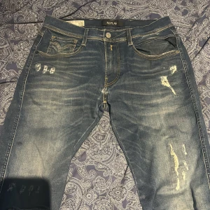 Replay Anbass Hyperflex jeans blå slim - Snygga Replay Anbass Hyperflex jeans i blå tvätt med slitningar och detaljerade sömmar. Slim fit-modell med klassisk femficksdesign, bruna läderpatch bak och coola slitna partier framtill. Perfekt för dig som gillar street och modern stil. Pris går o diskutera