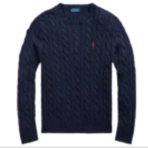 Marinblå stickad tröja från Ralph Lauren - Snygg marinblå stickad tröja från Ralph Lauren med klassiskt kabelstickat mönster och rund hals. Tröjan har lång ärm och den ikoniska röda Polo-loggan broderad på bröstet. Perfekt för dig som gillar stilrena och tidlösa plagg.