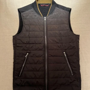 Svart dunväst från Zara  - Svart quiltad dunväst från Zara Man med dragkedja framtill och två snedställda fickor med dragkedja. Framsidan är lätt vadderad och baksidan är i mjukare tyg. Perfekt för lager-på-lager och stilren look.