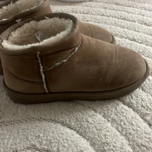 Bruna fodrade boots från Nelly - Mysiga bruna boots från Nelly med låg skaft och fluffigt vitt foder på insidan. Yttermaterialet är mockaliknande och sulan är rejäl med mönster för bra grepp. Perfekta för kalla dagar när du vill hålla fötterna varma.