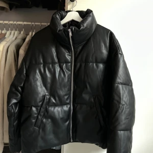 Svart boxig jacka - 🤍Svart boxig pufferjacka från Gina Tricot i storlek S. Jackan har en hög krage, quiltad design och är tillverkad i syntetmaterial med skinnlook. Den har dragkedja framtill och två snedställda fickor 🤍