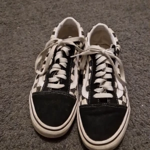 Vans Old Skool Checkerboard sneakers - Säljer ett par klassiska Vans Old Skool sneakers med svart och vit checkerboard-mönster. Skorna har vit sula, svarta detaljer i mocka på tå och häl, samt vita snören och den ikoniska sidoremsan. Perfekta för en cool streetstyle-look.