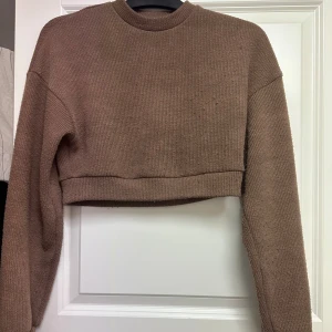 Brun croppad stickad tröja från SHEIN - Brun croppad stickad tröja från SHEIN i storlek XS. Tröjan har ribbad struktur, rund hals och långa ärmar.