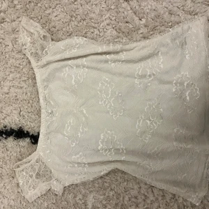 Vit spetsblus från Dorothy Perkins - Säljer en söt vit blus från Dorothy Perkins i storlek 36. Blusen har spetsdetaljer och ett blommigt mönster över hela tyget. Den är kortärmad med transparent spets vid axlarna och har en feminin, romantisk vibe. Perfekt för dig som gillar ljusa och eleganta toppar!