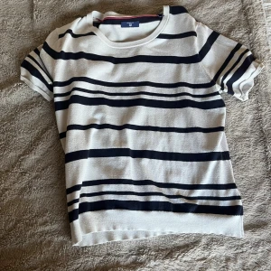 Randig vit och marinblå tröja från GANT - Snygg kortärmad tröja från GANT i vit med marinblå ränder. Rund halsringning och mjukt stickat material som känns skönt mot huden. 