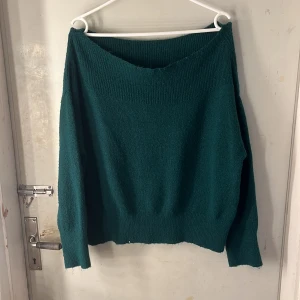 Mörkgrön stickad offshoulder tröja - Snygg mörkgrön stickad tröja med offshoulder-design och bred ribbad kant upptill. Perfekt för dig som gillar en chill och lite oversized look. Långärmad och mjuk, passar till jeans eller kjol för en cool vibe.
