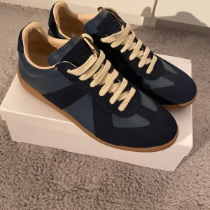 Maison Margiela sneakers  - Snygga sneakers från Maison Margiela i mörkblått skinn och mocka med beige snörning och gummisula. Klassisk siluett med rund tå och platt sula, perfekta för dig som gillar stilrena och exklusiva sneakers med en twist.