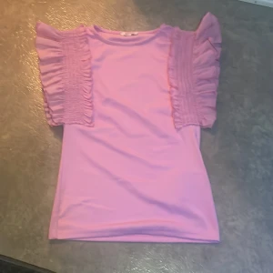 Rosa topp med volangärmar - Säljer en ljusrosa topp med korta, breda volangärmar. 