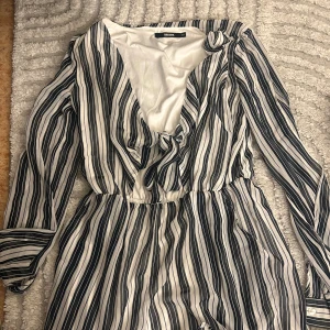 Randig omlottklänning från Bik Bok - Snygg kort omlottklänning från Bik Bok med svartvita ränder och knyt framtill. Klänningen har långa ärmar och resår i midjan för en bekväm passform. Tunt, luftigt material som känns lätt mot huden. Perfekt för dig som gillar en trendig och avslappnad stil.