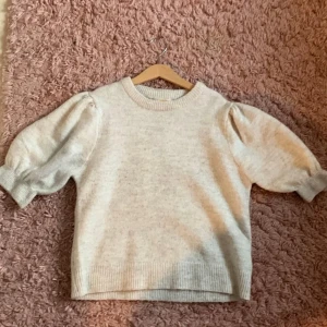 Beige stickad tröja från Gina Tricot - Superfin beige stickad tröja från Gina Tricot med puffiga ärmar och ribbade muddar. Tröjan har en klassisk rund halsringning och är perfekt för dig som gillar en enkel men trendig look.