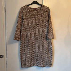 Mönstrad kortklänning från Indiska - Säljer en snygg kortklänning från Indiska i storlek M. Klänningen har ett geometriskt mönster i svart, brun och beige, med trekvartsärmar och rund hals. Materialet är mjukt och stickat, vilket gör den både bekväm och stilren. Perfekt för dig som gillar retrovibbar och coola prints.