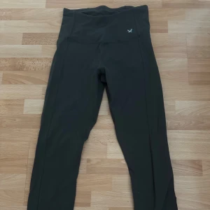 Tränning leggings från SOC med snörning - Grå/grön leggings från SOC i storlek S, tillverkade i ett stretchigt syntetmaterial med teknisk TCS Airflow-funktion. Hög midja och snygg snörningsdetalj baktill ger extra stilpoäng. Perfekta för träning eller chill. Diskret logga framtill.
