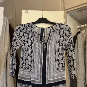 Blåvit mönstrad blus - Säljer en blåvit blus som har trekvartsärm och knytning vid halsen. Perfekt för dig som gillar boho-vibe och vill ha något unikt i garderoben.