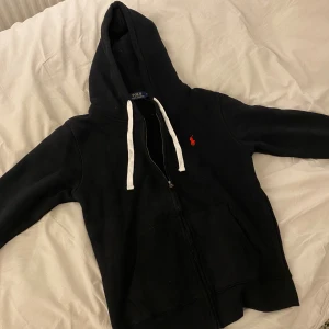 Svart Ralph Lauren Zip Hoodie  - Säljer denna otroligt snygga Ralph Lauren zip hoodien i svart. Finns inga defekter eller liknande och knappt använd. Säljer pga att den är för liten för mig. Hör av dig om du undrar något🤝😃