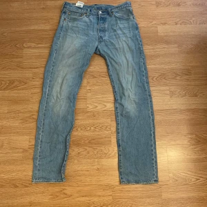 Levi's 501 ljusblå jeans W32 L32 - Klassiska Levi's 501 jeans i ljusblå tvätt med raka ben och knappgylf. Jeansen har fem fickor, brunt läderpatch bak och den ikoniska röda Levi's-taggen vid bakfickan. 