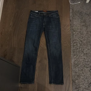 Mörkblå jeans Jack & Jones Clark - Snygga mörkblå jeans från Jack & Jones, modell Clark. Klassisk femficksdesign med raka ben och normal passform. Jeansen har en cool tvättad look och är tillverkade i slitstarkt denimtyg. Perfekta för dig som gillar stilrena och tidlösa jeans.