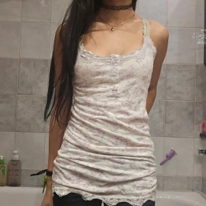 Blommig spetskantad linnetopp - ❗️Skriv innan köp❗️Vitt linne från Cubus i storlek XS. Ljus botten med lila blommigt mönster, tunna axelband och spetsdetaljer vid halsringning och nederkant. Finns några slitna trådar och har används. 