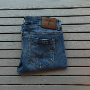 Blå jeans från Dondup med raka ben - Snygga blå jeans från Dondup med klassisk femficksdesign och raka ben. Jeansen har en ljus tvätt, bruna sömmar och en läderpatch med logga bak i midjan. Materialet är mjukt jeans och passformen är normal. Perfekt för dig som gillar stilrena och tidlösa jeans.