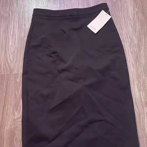 Svart långkjol från Zara Basic - Snygg svart långkjol från Zara Basic med stilren och rak passform. Kjolen har en klassisk design utan synliga detaljer och passar perfekt till en trendig och minimalistisk look. Materialet känns mjukt och följsamt mot kroppen.