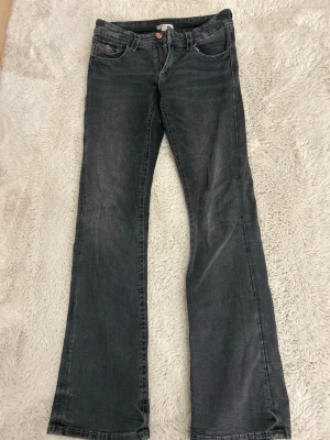 Grå bootcut jeans med broderade fickor - Snygga grå svarta jeans med bootcut passform och broderade detaljer på bakfickorna. Klassisk model med knapp och dragkedja framtill. Jag säljer dem här jeansen för att den har blivit för korta för mig, jag är ungefär 1,74 cm lång. Jag har använt dem mycket och man ser de men det är inget större fel på dem.