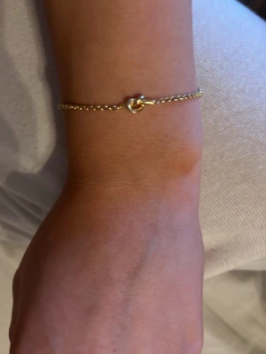 Guldfärgat armband med knutdetalj - Snyggt och minimalistiskt armband i guldfärgad metall med en tunn kedja och en stilren knutdetalj i mitten. Perfekt för dig som gillar enkel och trendig design. Armbandet har ett smidigt lås och passar till många olika stilar. Vet tyvärr inte vart det är ifrån då jag fick det i födelsedagspresent