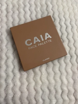 CAIA Face Palette Classy - Säljer en CAIA Face Palette i färgen Classy. Paletten innehåller fyra olika nyanser för ansikte: blush, bronzer och highlighter i varma, naturliga toner. Kommer i en fyrkantig brun förpackning med spegel i locket. Perfekt för att skapa en fräsch look.