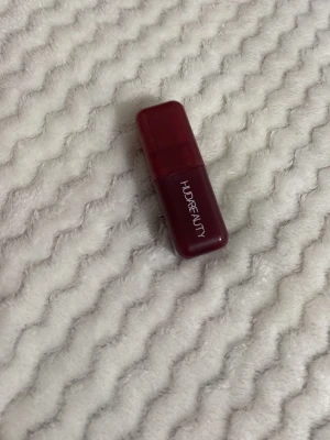 Huda Beauty Black Cherry Blush - Flytande rouge från Huda Beauty i färgen Black Cherry. Kommer i en kompakt, fyrkantig förpackning i mörkröd plast med vit logga. Perfekt för att ge kinderna en djup bärig ton och ett fräscht glow.