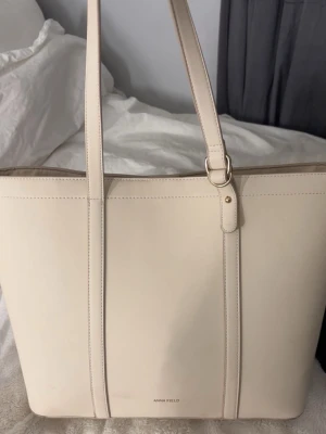 Beige väska från Anna Field - Stilren och rymlig shoppingväska från Anna Field i beige syntetmaterial. Väskan har långa axelband och minimalistisk design med diskreta gulddetaljer. Perfekt för att bära allt du behöver under dagen. Se defekter på bild två, lite går att rengöra