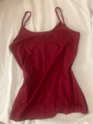 Röd linnetopp med smala axelband - Snygg röd linnetopp med smala axelband och enkel design. Perfekt att matcha med jeans eller kjol för en trendig look. Tunt och mjukt material som känns skönt mot huden.