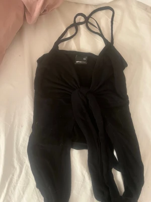 Svart knyt topp från Ginatricot - Trendig svart topp från Ginatricot med smala axelband och snygg knytning framtill. Toppen är ärmlös och croppad, perfekt att styla med höga jeans eller kjol. Enkel men ändå statement med sin knutdetalj och figurnära passform.