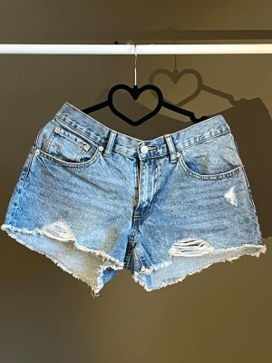 Blå lågmidjade jeansshorts med slitningar - Snygga blå jeansshorts med råa kanter och slitna detaljer framtill. Klassisk femficksmodell med knapp och dragkedja. Lågmidjade. Perfekta för varma dagar och en avslappnad stil. Köpt från Lager 157, aldrig använda🐚💙