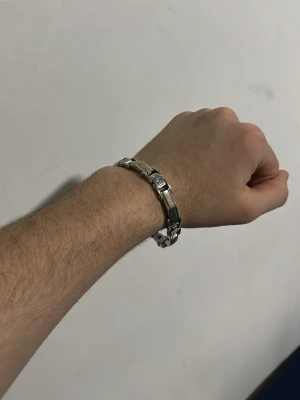 Stilrent länkat armband i metall - Säljer ett snyggt armband i silverfärgad metall med guldfärgade detaljer. Armbandet har en länkdesign med rektangulära sektioner och ett smidigt spänne. Perfekt för dig som gillar en clean och modern look.