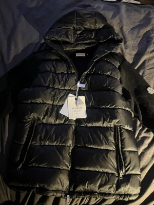 Moncler cardigan - Snygg svart dunjacka/fleece från Moncler med huva och stickade ärmar. Helt ny aldrig använd med prislapparna kvar. Säljer då jag måste bli av med min garderob. Storlek 3/M