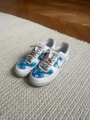 Nike Air Force 1 custom-made, blå/vit - Unika Nike Air Force 1 sneakers med custom-made inspirerat blått och vitt mönster på tå och sidor. Skorna är låga med vit bas, blå detaljer och klassisk snörning. Perfekta för dig som vill sticka ut med en riktigt snygg och trendig look.
