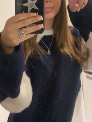 Mörkblå och vit stickad tröja  - Säljer en  tröja i mörkblått med vita partier på ärmarna. Tröjan har en avslappnad passform och rund halsringning. Perfekt för en chill och trendig look.