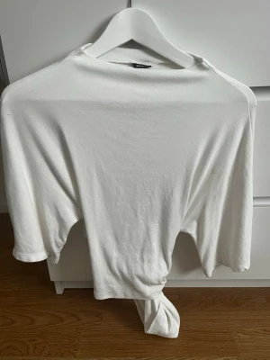 Vit croppad topp med knyt - Säljer en vit croppad topp med knyt framtill. Toppen har trekvartsärm och är tillverkad i mjukt bomullsmaterial. Enkel och clean design som passar perfekt till jeans eller kjol. Perfekt för dig som gillar minimalistisk stil.