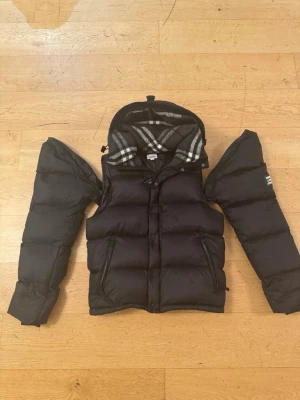 Burberry Jacka Väst - Svart dunjacka från Burberry med avtagbara ärmar. Helt oanvänd. Köpt från butik för ca 2 år sen men nästa aldrug kommit till användning. Ej min stilo 