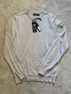Stickad ljusbeige ulltröja J.Lindeberg - Helt ny stickad J. Lindeberg tröja. Köptes ny för ca en månad sedan för  2199kr. Säljer den nu till ett väldigt bra pris. Först till kvarn! 